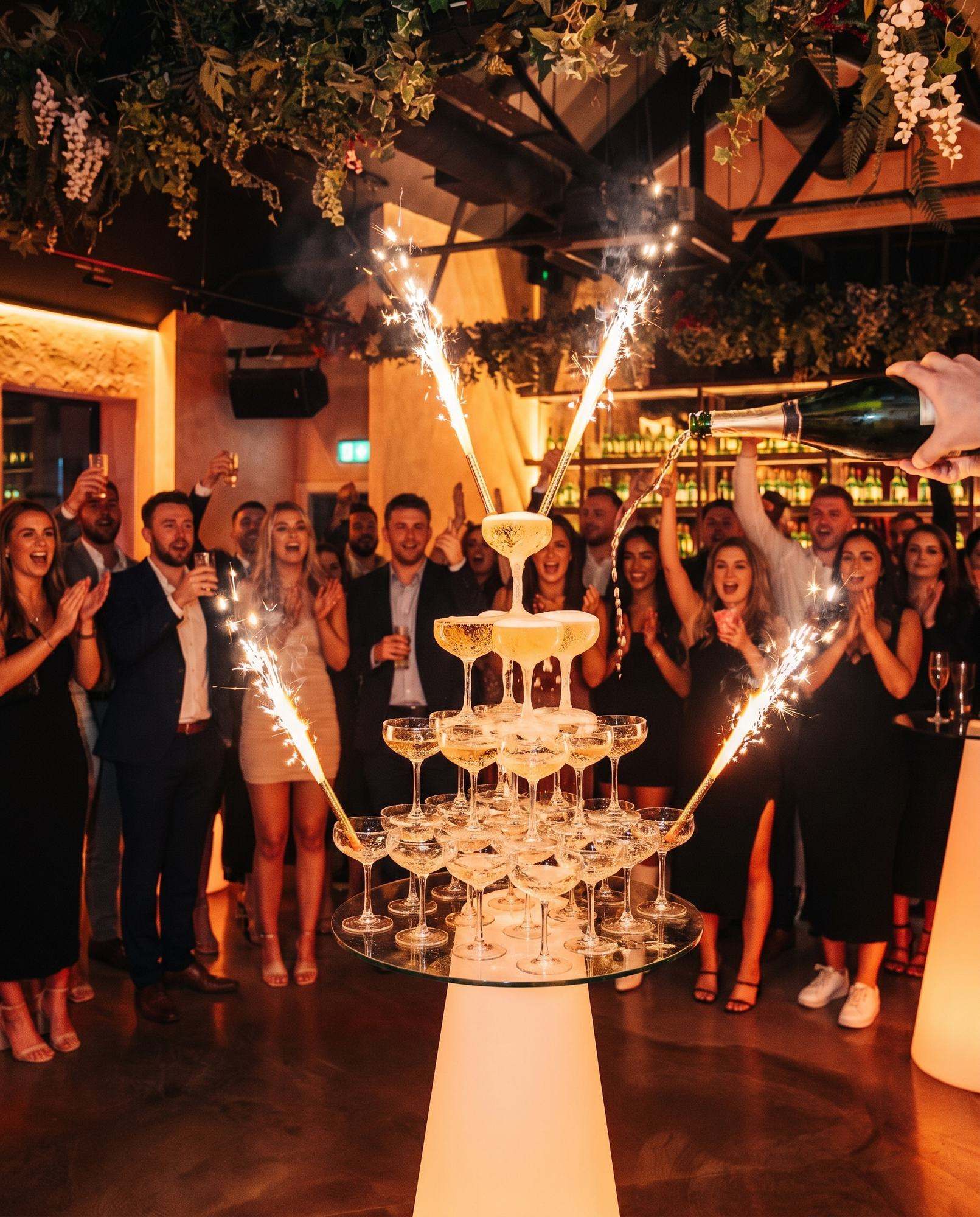A champagne tower poured at a birthday, sparklers lit